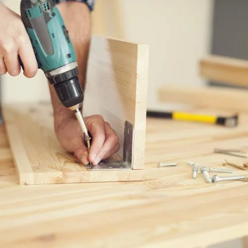 reforçando moveis Montador de móveis profissional utilizando parafusadeira elétrica para fixar cantoneira de ferro em prateleira. Serviço técnico com ferramentas adequadas e precisão.